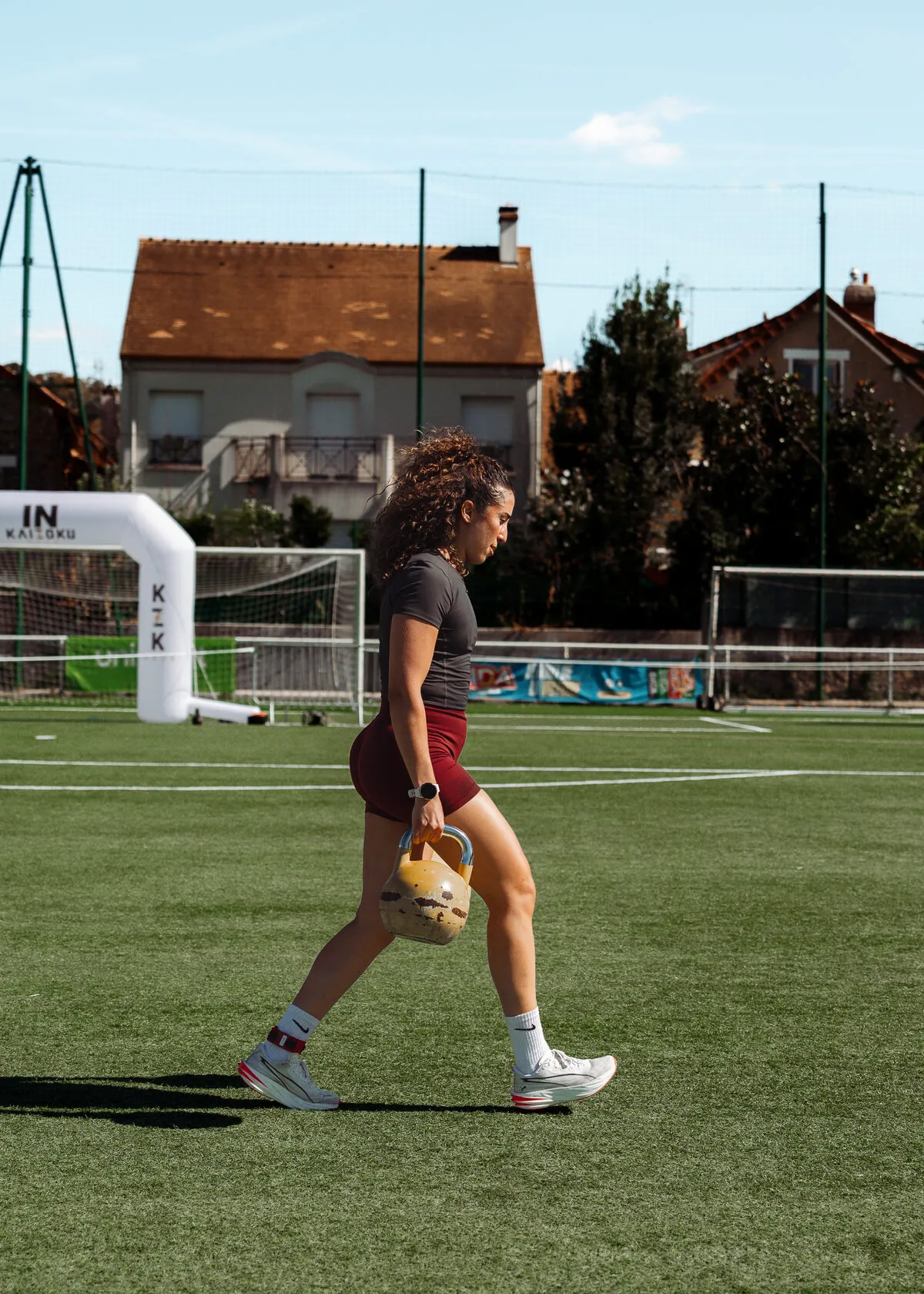 Une athlète en farmer carry, kettlebell à la main, devant l'arche gonflable de la course
